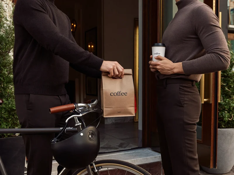 Kurier auf dem Fahrrad übergibt Kaffeetüte und Becherträger an der Wohnungstür